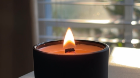 Luxury black candle burning in soft natural daylight with wooden wick and calming flame — minimalist quiet luxury home fragrance atmosphere. Grice Wax & Wicks