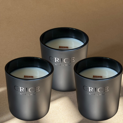 A slow burning luxury candle in a matte black vessel with a wooden wick, hand-poured by Grice Wax & Wicks. Photographed in natural light with soft shadows on a warm neutral background.