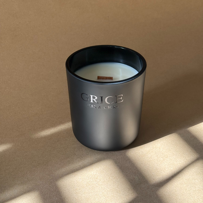 A slow burning luxury candle in a matte black vessel with a wooden wick, hand-poured by Grice Wax & Wicks. Photographed in natural light with soft shadows on a warm neutral background.