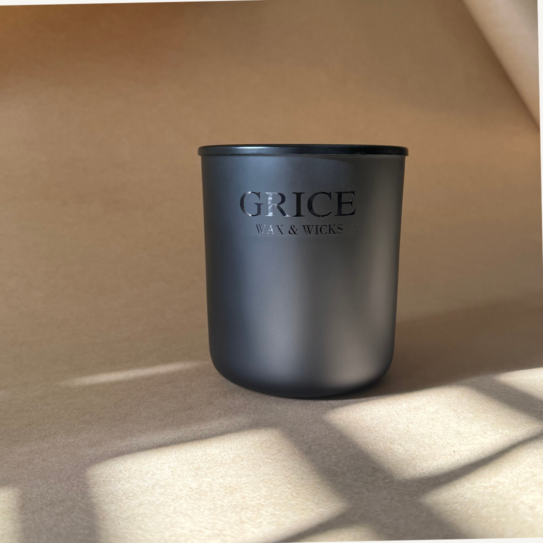 A slow burning luxury candle in a matte black vessel with a wooden wick, hand-poured by Grice Wax & Wicks. Photographed in natural light with soft shadows on a warm neutral background.