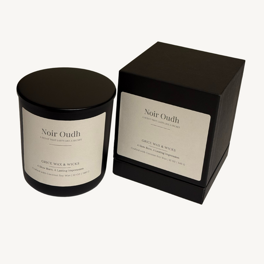 Candle labeled ‘noir oudh’ in a matte black vessel, surrounded by rich textures and deep shadows, evoking a bold, smoky blend of oud, amaretto and oud. 
