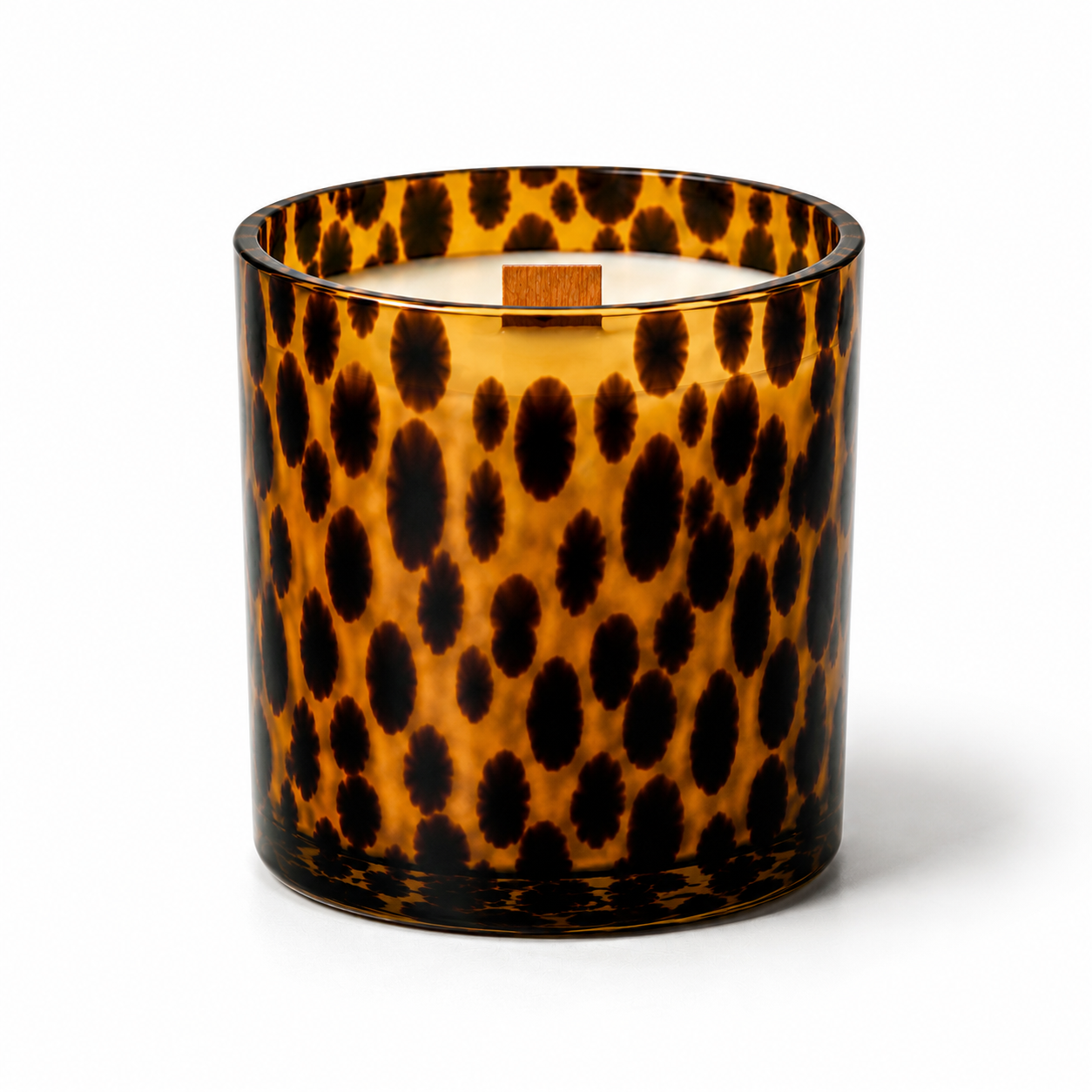 A candle in a clear glass jar with a bold leopard print pattern in amber brown and black, featuring white wax and a small wooden label on top, set against a plain white background.
