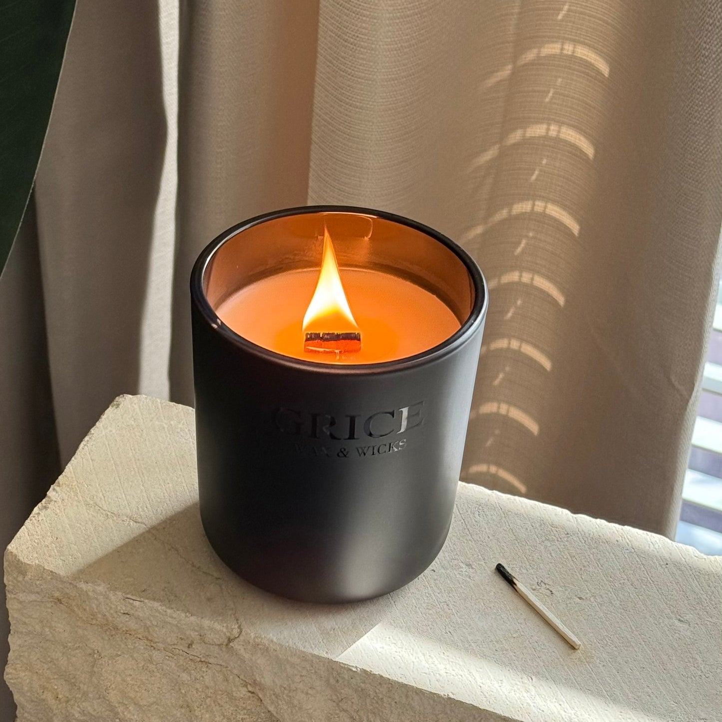 Black candle with a lit flame on a stone surface with a neutral curtain background