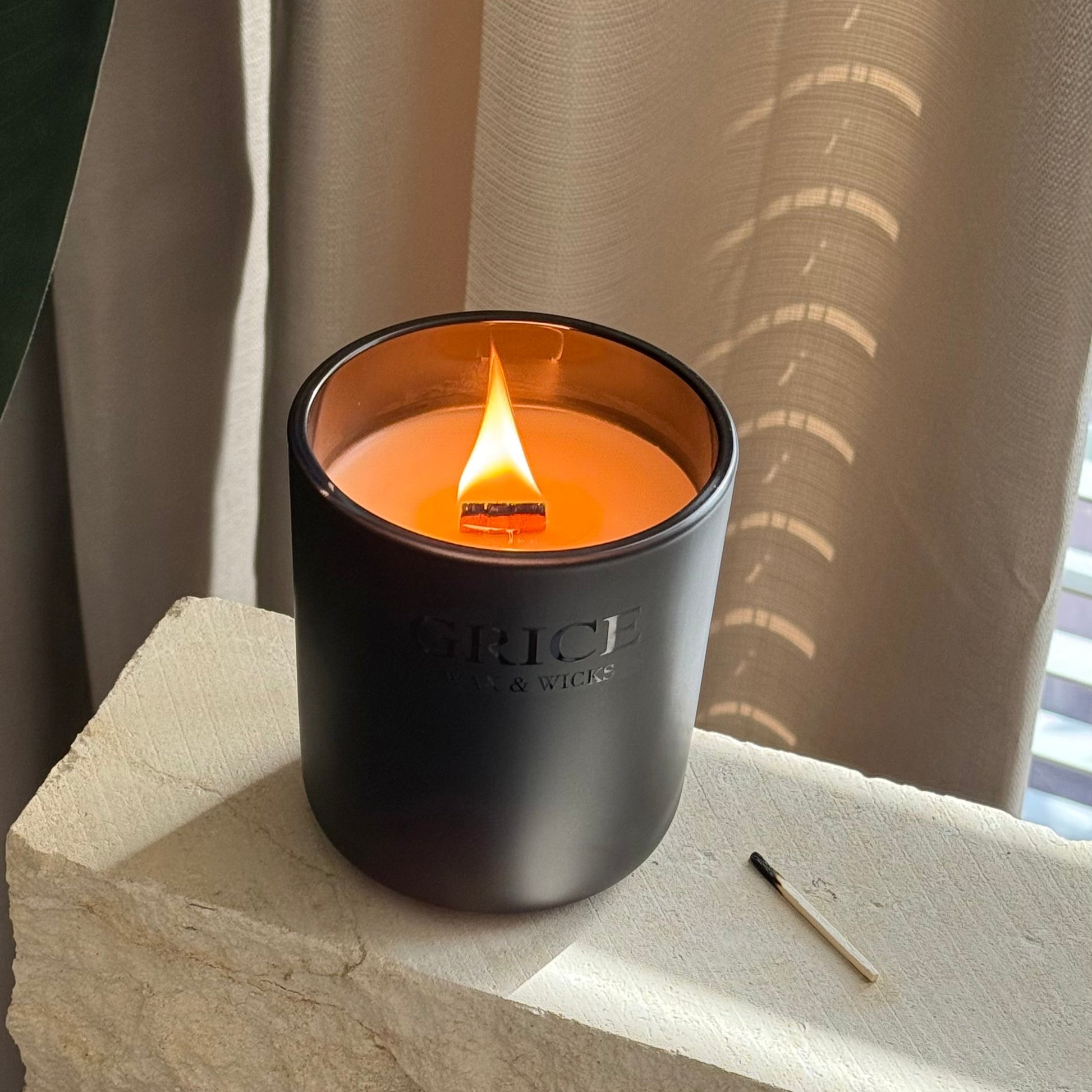 Black candle with a lit flame on a stone surface with a neutral curtain background