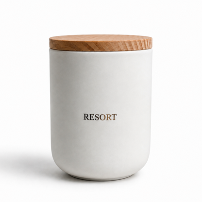 A white ceramic jar with a light brown wooden lid, featuring the word 'RESORT' printed in black on the front, set against a plain white background.