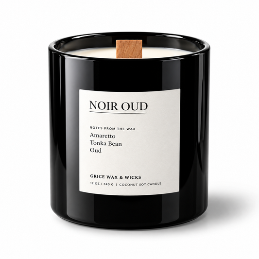 A black glass jar candle with a white label reading 'NOIR OUD' and a small wooden wick, photographed on a clean white background.