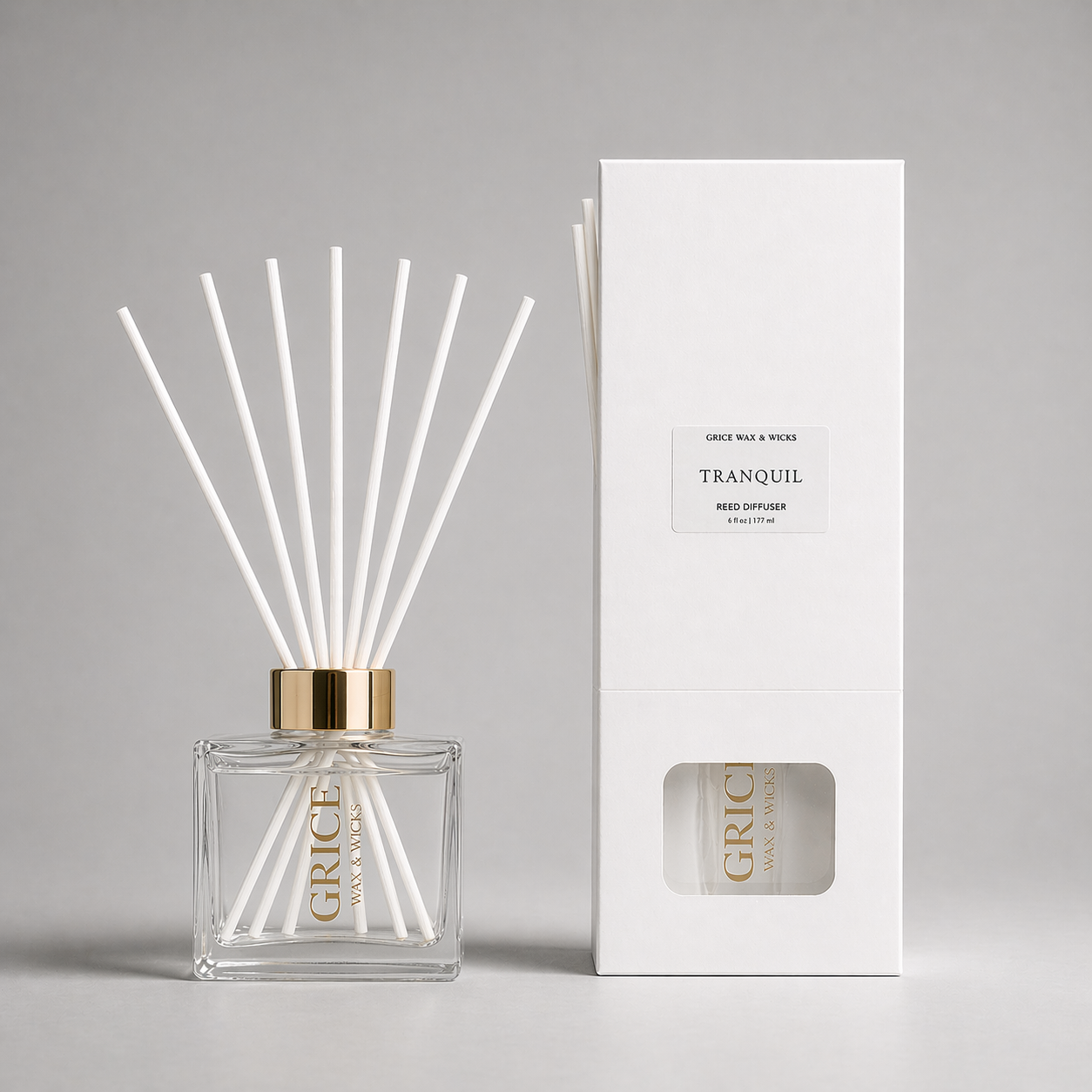 Reed diffuser with white sticks and gold cap next to its packaging on a gray background