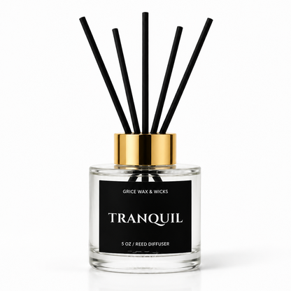 A 5 oz reed diffuser bottle with a clear glass body, black label, and gold collar, featuring six black reed sticks, on a white background.