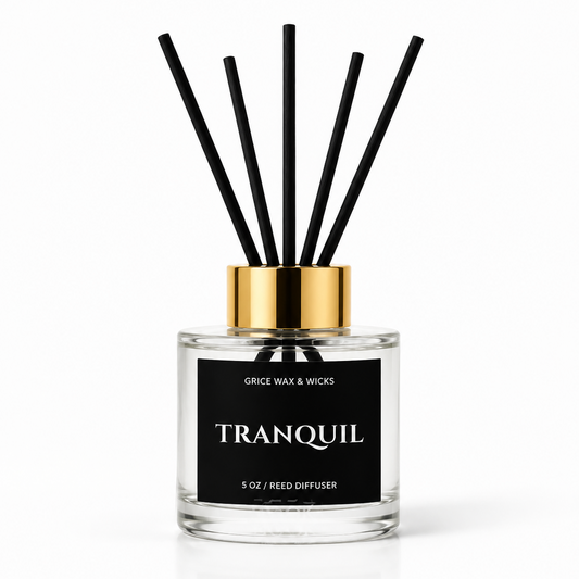 A 5 oz reed diffuser bottle with a clear glass body, black label, and gold collar, featuring six black reed sticks, on a white background.